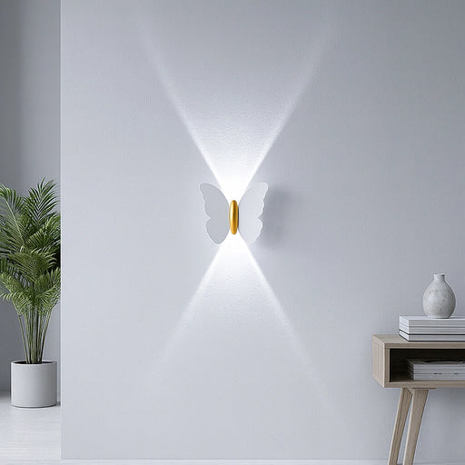 Butterfly-shaped wall light fixture on a white wall with a plant and side table in the foreground.