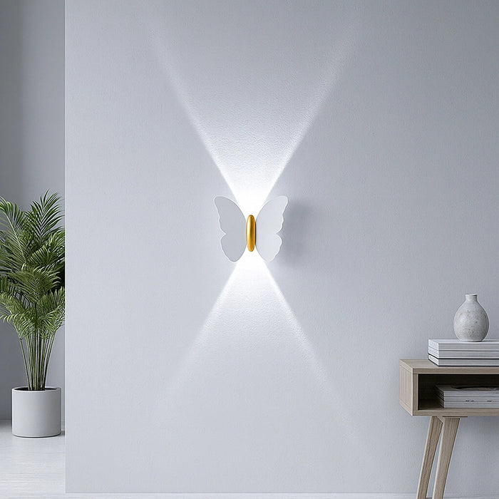 Butterfly-shaped wall light fixture on a white wall with a plant and side table in the foreground.