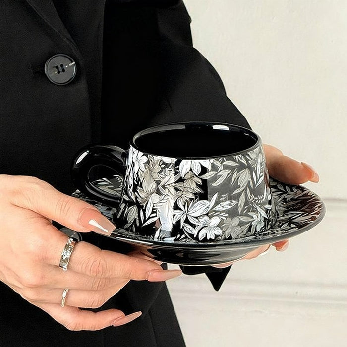 Person holding a black and white floral teacup and saucer set.