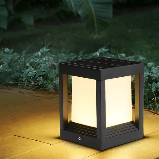 Black outdoor solar lamp on a patio with greenery in the background