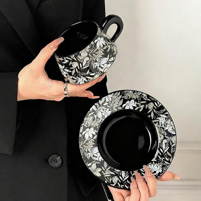 Person holding a black and white floral-patterned teacup and saucer set.