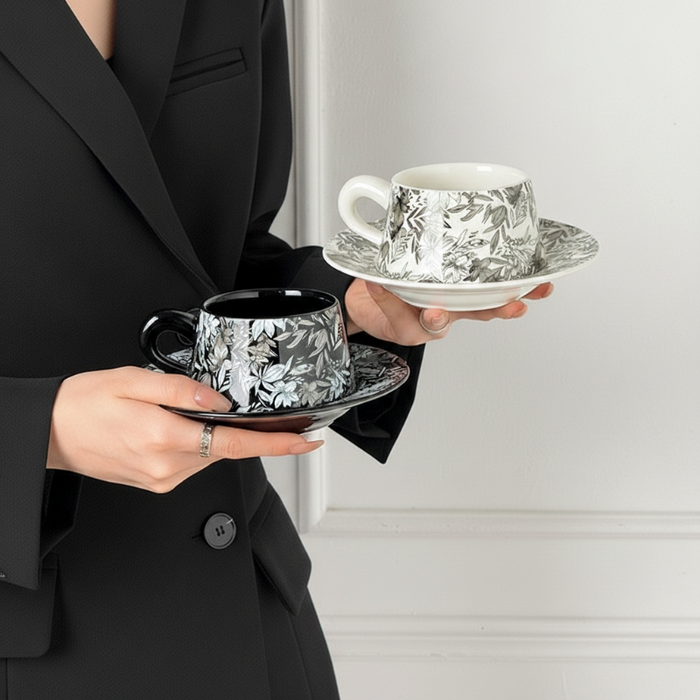 Person holding two floral teacups and saucers for the Botanica Porcelain Cup Saucer Set