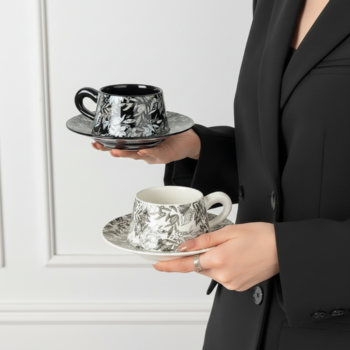 Person holding two patterned teacups on saucers for the Botanica Porcelain Cup Saucer Set