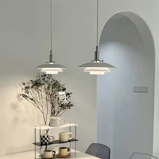 Two pendant lights hanging above a table with a plant and cups in a modern interior setting.