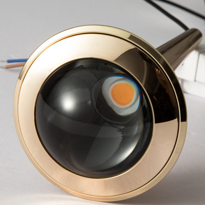 Close-up of a gold-framed black object with an orange center on a light gray background