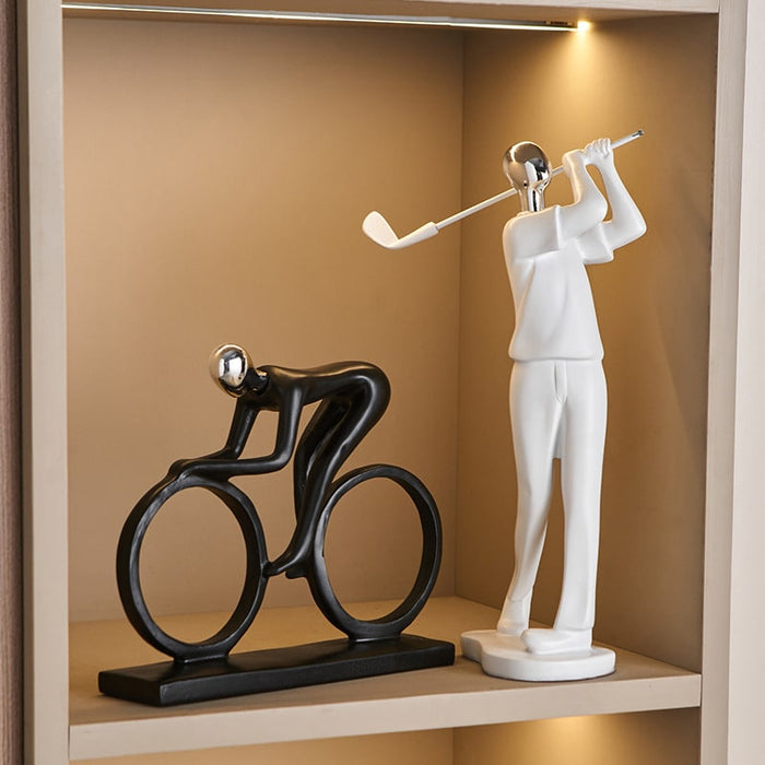 Decorative statues of a cyclist and a golfer on a shelf with a warm background