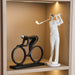 Decorative statues of a cyclist and a golfer on a shelf with a warm background