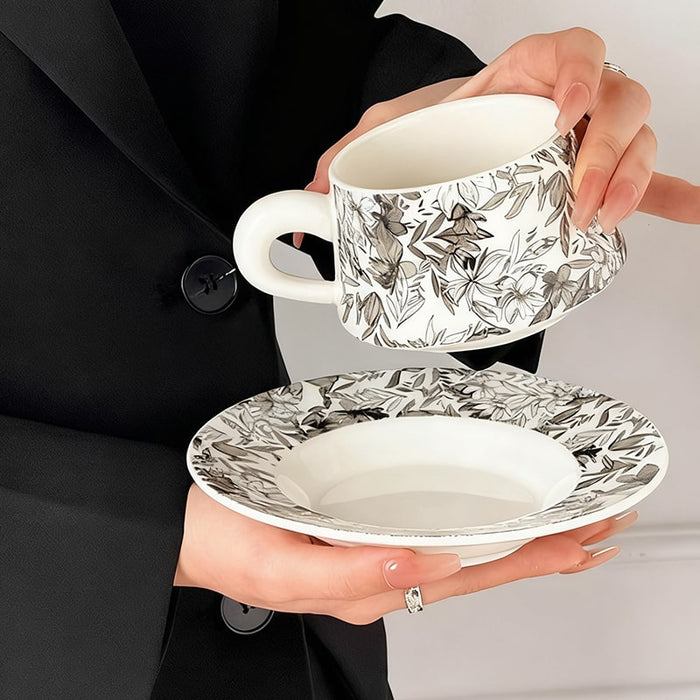 Person holding a floral-patterned teacup and saucer set.