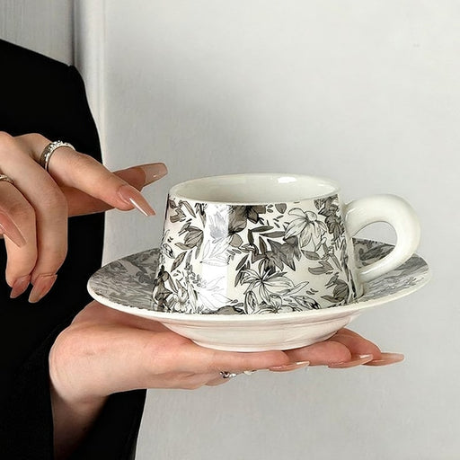 Person holding a floral-patterned teacup and saucer against a plain background